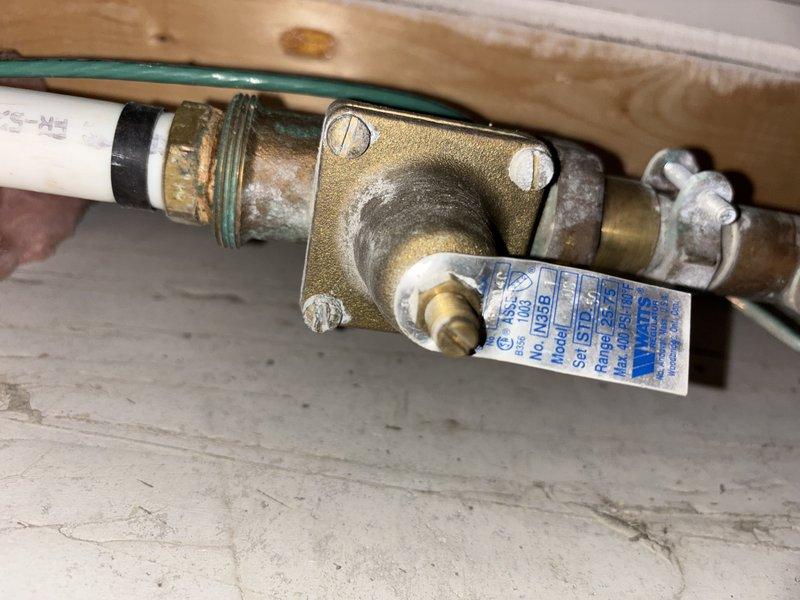 Inspected the plumbing supplying the tanked water heater in response to a reported pipe leak and found corrosion and mineral buildup (verdigris and scale) at the brass fittings on both sides of the pressure-reducing valve, indicating a leak point at the threaded joint and clamped connection. Verified system pressure with an analog gauge at approximately 50 psi, within normal operating range. Documented the condition of the fittings and recommended repair or replacement of the corroded connections to prevent further leakage.