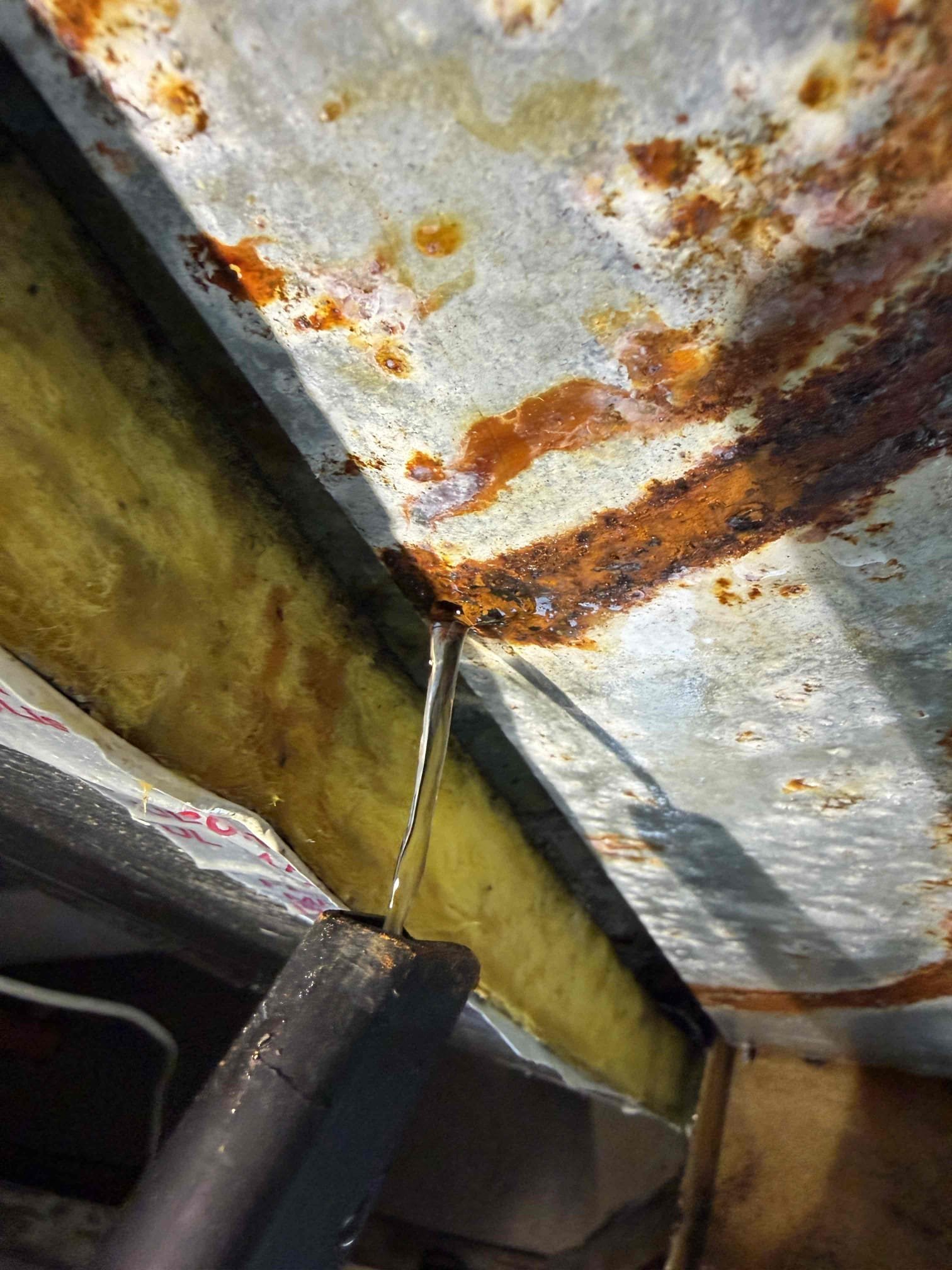 Upon my inspection, found that the bottom of the evaporator has three drain holes that are plugged up with rust debris. 
Performed a deep cleaning on these holes that required taking the drain system completely off of the unit. This is out of the scope of a Maitenence. Performed repair and system now drains properly. If issue persists, we will need to replace either the bottom piece of metal on the evaporator coil or replace the system. 