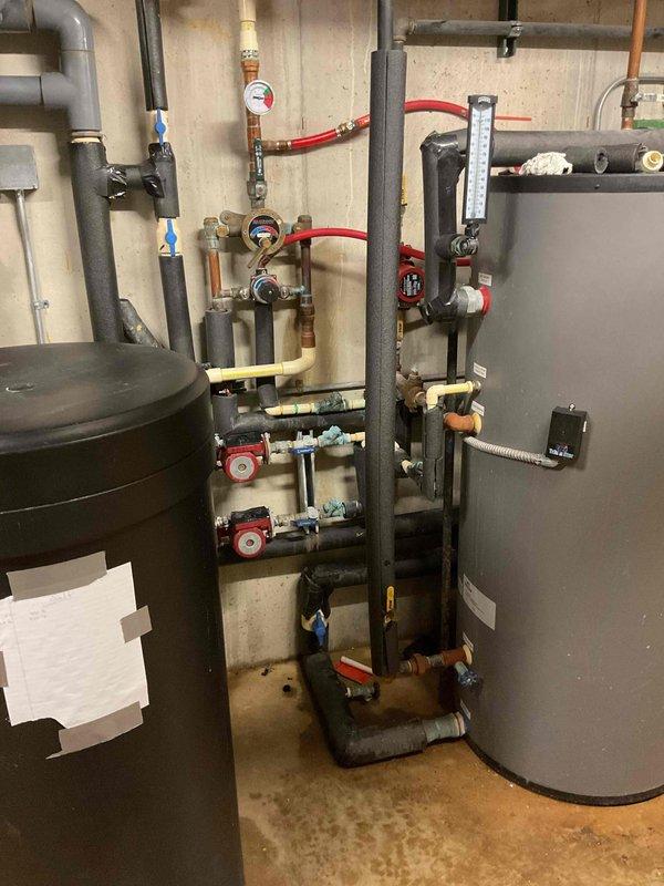 Responded to service call for boiler with no hot water production. Upon inspection, determined boiler was severely limed up causing operational failure. System appeared to have proper installation with two tanks connected by intricate piping network and multiple pressure gauges.