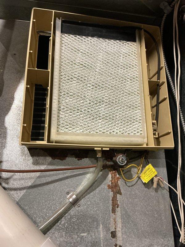 Responded to service call regarding detached Aprilaire humidifier. Inspection revealed the unit had fallen from mounting on furnace, causing damage to the housing and internal components. Observed significant rust/corrosion on the metal surface beneath the installation point. Recommended complete replacement of the humidifier rather than repair due to extent of damage and compromised mounting area.