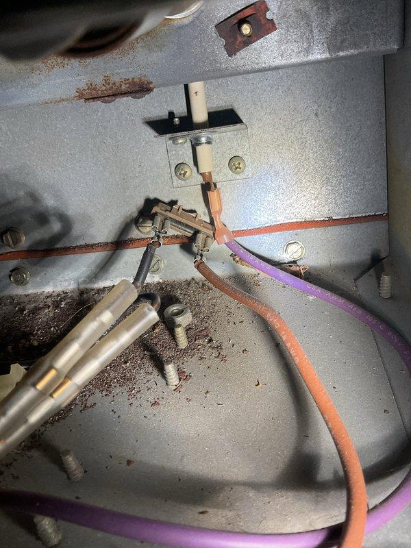 Responded to no-heat call and inspected furnace system located in partially converted basement storage area. Identified significant corrosion and rust on electrical terminal connections, with particular attention to damaged purple and orange wiring at connection points. Noted unsafe storage conditions with clothing and personal items placed directly against furnace unit and blocking proper airflow.