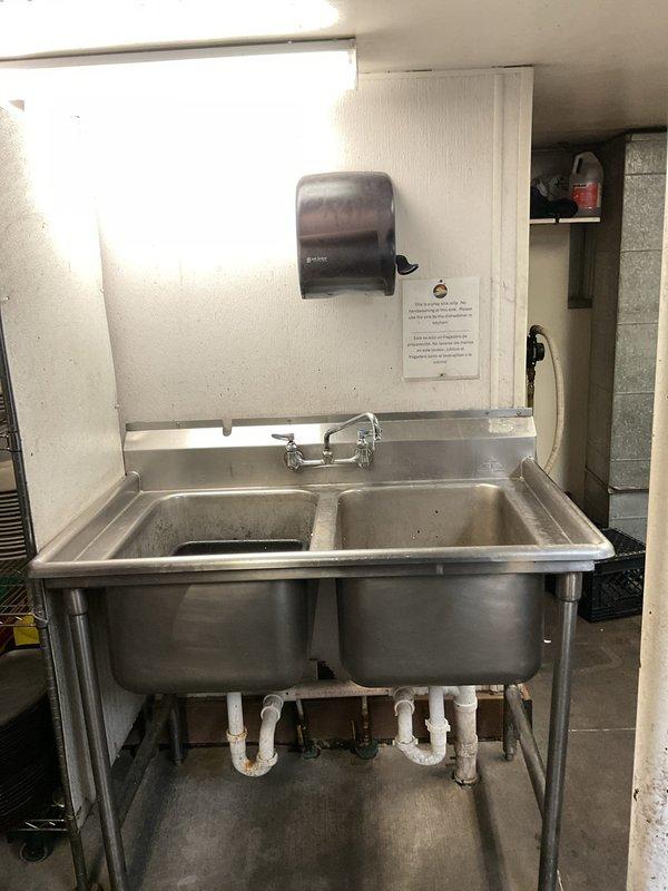 Responded to service call for non-operational wall-mounted air conditioning unit and air current issues near front entrance. Inspected and assessed HVAC system performance. Additionally addressed two dripping sink faucets in commercial double-basin stainless steel sink unit, identifying worn valve components causing leaks at both hot and cold water handles.