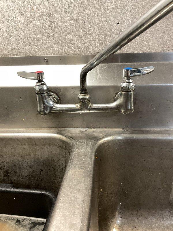 Responded to service call for non-operational wall-mounted air conditioning unit and air current issues near front entrance. Inspected and assessed HVAC system performance. Additionally addressed two dripping sink faucets in commercial double-basin stainless steel sink unit, identifying worn valve components causing leaks at both hot and cold water handles.