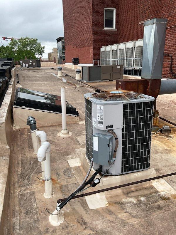 Responded to service call for leaking rooftop AC unit located on commercial building fifth floor, accessed through YWCA facility with tenant code assistance. Upon inspection, found white HVAC condensing unit with weathered components and visible rust on fan grille, connected to black refrigerant lines and gray electrical disconnect. Identified condensate drainage issue with white PVC piping system showing discoloration at roof membrane interface. Documented rooftop equipment configuration including multiple commercial air handling units and assessed condition of refrigerant line connections and condensate management system to address reported water leakage.