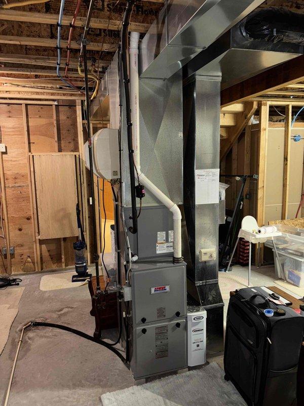 Responded to service call for furnace inspection in residential basement. Upon arrival, coordinated appointment time with homeowner and confirmed scheduling details. Performed comprehensive visual inspection of gas furnace system and associated HVAC components. Examined furnace unit, verified proper installation and mounting on concrete pad, and inspected manufacturer labeling and identification plates. Assessed ductwork connections including main supply plenum and branch distribution runs throughout ceiling joists. Verified proper sealing and support of sheet metal ductwork. Inspected condensate drainage system including white PVC piping and routing. Checked electrical connections and service panel accessibility. Evaluated overall system installation quality in unfinished basement space with exposed framing. Confirmed furnace operational readiness and proper integration with existing duct distribution network. Documented system condition through photographic records showing furnace un
