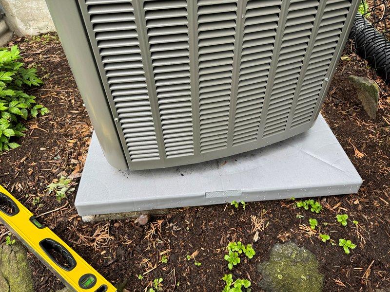 Responded to warranty call for recently installed A/C unit experiencing slab displacement due to soil washout causing equipment to slide and pull away from structure. Stabilized unit by placing rock material in front of and underneath equipment to prevent further movement. Verified level placement of unit on pad after stabilization, though noted that washout conditions may recur without additional permanent measures such as enhanced drainage or expanded stone base.
