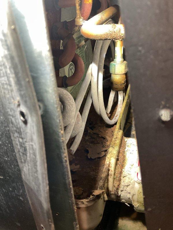 Responded to no cooling complaint with system running but not cooling and weak airflow. Upon inspection, found evaporator coil severely iced over due to restricted airflow and evidence of refrigerant system issues. Manifold gauge readings confirmed low suction pressure at 18.3 PSI with abnormal temperature differentials. Observed heavily corroded copper refrigerant lines with deteriorated insulation and significant moisture intrusion at outdoor unit connections. System exhibited classic symptoms of low refrigerant charge combined with restricted airflow across evaporator coil. Documented equipment condition with photos showing extensive frost accumulation on suction line and corroded piping requiring attention.