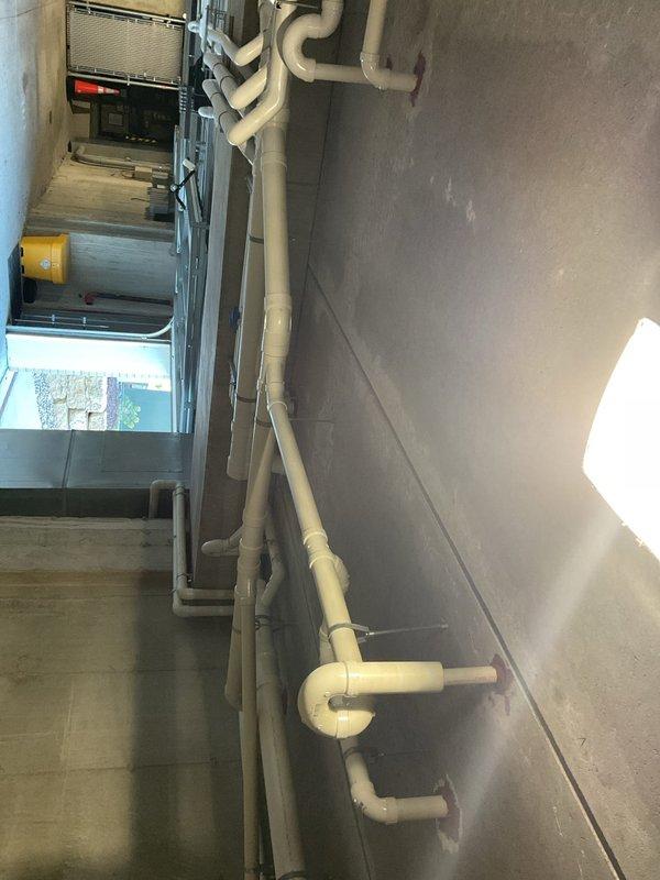 Responded to complaint of mini split head unit leaking water from both corners at random intervals throughout the day. Folded up mini split head to access internal components and inspected drain hose assembly on backside of unit. Located drain hose inside unit and loosened 5/16 clamp securing drain line. Cleared blockage by blowing out drain hose, removing obstruction that was preventing proper condensate drainage. Drain line now flowing freely on backside of unit, resolving water discharge issue.