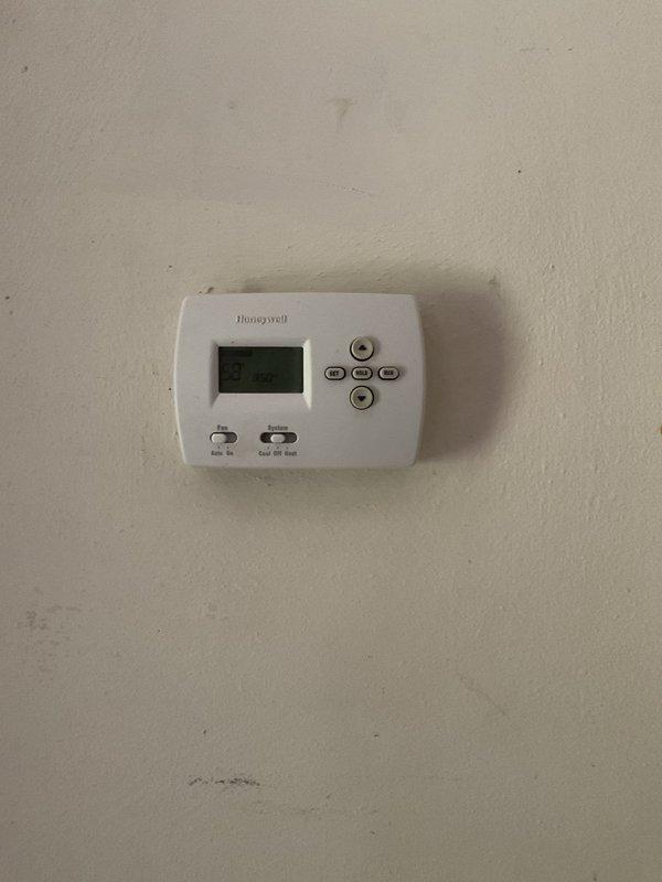 Responded to service call for air conditioning system not operating at vacant property. Upon arrival, accessed unit using provided lockbox code and performed diagnostic assessment of outdoor condenser unit and indoor thermostat controls. Inspected outdoor condensing unit positioned against exterior wall, verified electrical connections at disconnect box, and examined conduit routing from unit to wall-mounted disconnect. Checked indoor Honeywell digital thermostat for proper settings and functionality. System evaluated and photographed for documentation purposes.