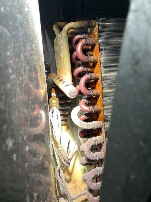 Responded to no-cool call with reported water dripping from indoor unit and ice formation on outdoor condenser. Upon arrival, found system shut down by customer due to active leak. Inspection revealed evaporator coil severely restricted with dirt and debris accumulation, causing refrigerant pressure drop and ice buildup on both indoor and outdoor components. Photographed corroded evaporator coil showing significant oxidation on copper tubing and reduced airflow through heat exchanger fins. Advised customer that restricted airflow from dirty coil caused system to freeze, resulting in condensate overflow when ice melted. Recommended professional coil cleaning or possible coil replacement due to age and corrosion level observed during inspection.