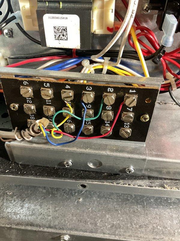 Responded to no-heat call on water source heat pump system following previous technician's diagnosis of suspected control board failure. Inspected electrical connections at terminal block and transformer assembly, verifying wire terminations at numbered terminals and thermostat base plate. Documented wiring configuration including R, W, Y, G, and AUX terminals on UWP16 control, with all low-voltage connections intact at both unit and wall-mounted thermostat locations.