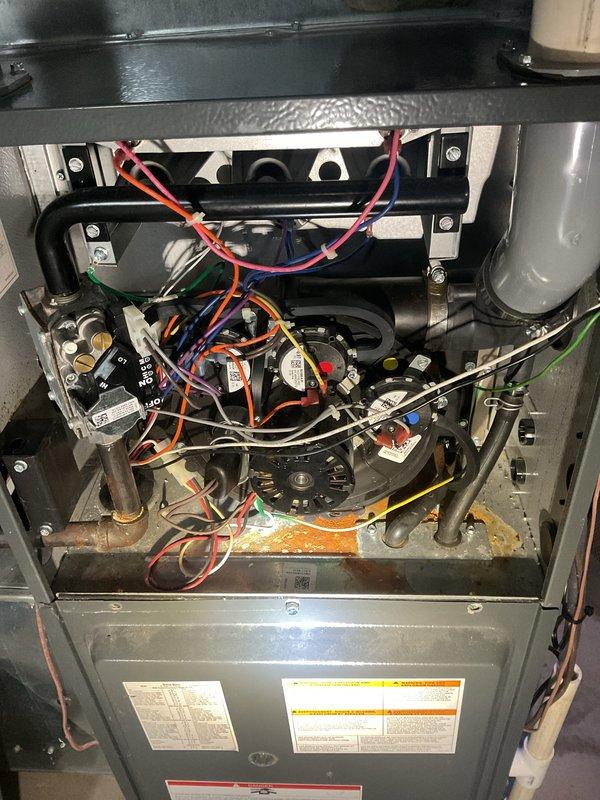 Responded to service call for furnace system installed in 2021 experiencing internal rust and leaking issues. Upon inspection, accessed furnace interior and documented significant corrosion on base plate with yellowish-orange discoloration indicating moisture intrusion and rust buildup. Examined burner assembly, electrical connections, gas lines, and sensor components throughout the unit. Inspected exterior condensate drainage system and PVC venting configuration mounted on building exterior. Assessment revealed lack of consistent annual maintenance history contributing to premature deterioration of internal components. Documented all findings with photographs for warranty review and recommended immediate attention to address leaking issue and corrosion damage to prevent further system degradation.