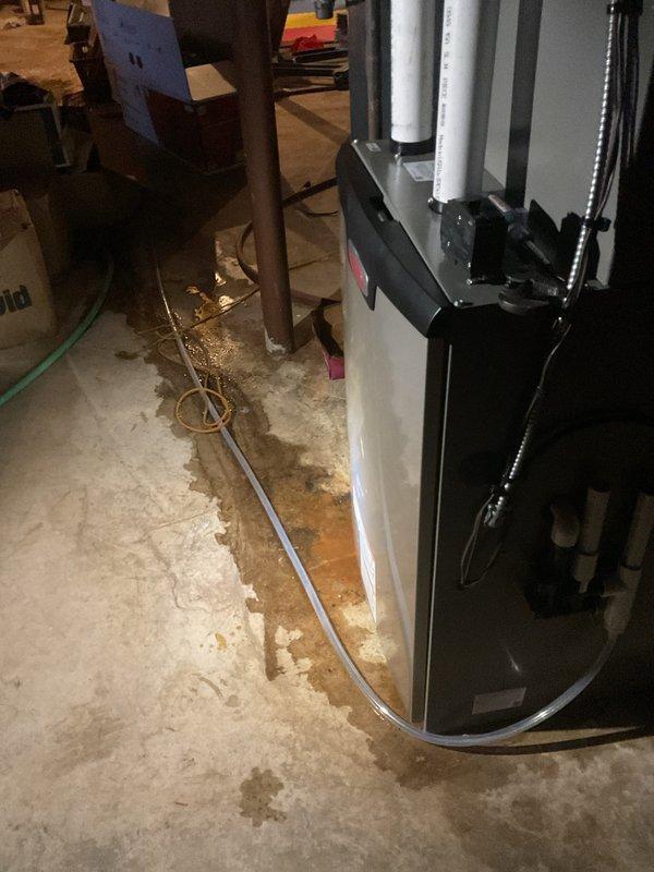Inspected the high-efficiency condensing furnace and identified water staining and standing moisture on the floor at the base of the unit, along with mineral deposits indicating a recurring condensate leak. Evaluated the condensate drain assembly, including the PVC drain piping, tee fitting, and condensate pump, and verified the drain line and fittings were intact with no visible damage or corrosion. Reviewed thermostat operation with the homeowner, demonstrating programming, mode selection, and temperature setpoint adjustments.
