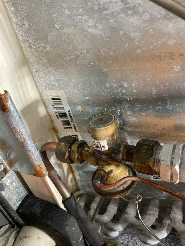 Responded to a furnace water leak complaint and found the condenser coil heavily soiled. Cleaned the condenser coil and ran the system to verify operation. Noted corrosion on the brass refrigerant service valve and fittings, along with rust and moisture staining on the surrounding cabinet panels.