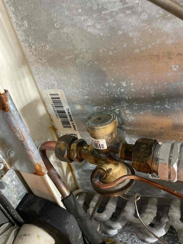 Responded to a furnace water leak complaint and found the condenser coil heavily soiled. Cleaned the condenser coil and ran the system to verify operation. Noted corrosion on the brass refrigerant service valve and fittings, along with rust and moisture staining on the surrounding cabinet panels.