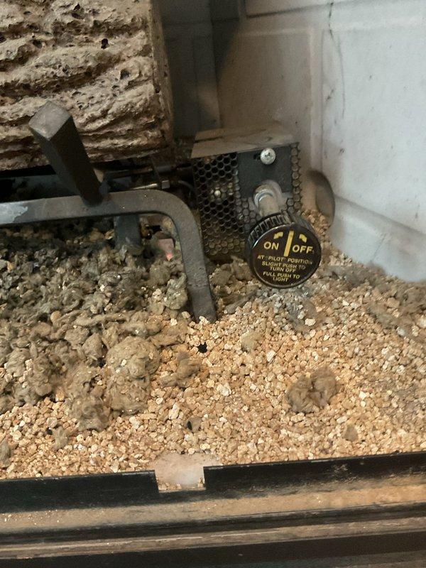 Performed a gas fireplace tune-up and inspected the firebox, burner assembly, log set, and pilot control valve. Found significant dust, lint, and debris accumulated across the vermiculite media and around the burner, which can restrict airflow and cause low pilot flame and gas bleed-through after shutoff. Documented the pilot control valve operation and the debris buildup, and recommended further evaluation for a replacement gas valve or log/burner assembly if pilot and shutoff issues persist.