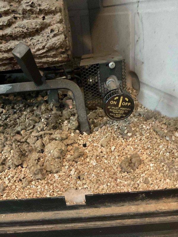 Performed a gas fireplace tune-up and inspected the firebox, burner assembly, log set, and pilot control valve. Found significant dust, lint, and debris accumulated across the vermiculite media and around the burner, which can restrict airflow and cause low pilot flame and gas bleed-through after shutoff. Documented the pilot control valve operation and the debris buildup, and recommended further evaluation for a replacement gas valve or log/burner assembly if pilot and shutoff issues persist.