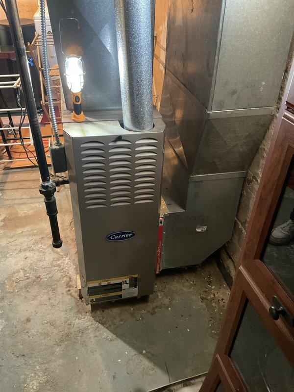 Performed a complete heating system tune-up on an 11-year-old Carrier upright furnace, inspecting the cabinet, flue venting, and supply ductwork for proper connections and condition. Noted surface corrosion and weathering on sections of the galvanized round ductwork and flue, which should be monitored for future sealing or replacement. The furnace was operated through a heating cycle to verify proper function, and the unit is in operational condition following the maintenance.