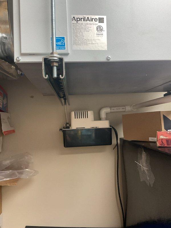 Responded to a reported clanking noise on an AprilAire Model E130 dehumidifier suspended from overhead strut channel and threaded rod. Inspected the unit, mounting hardware, condensate tubing, and condensate pump with PVC discharge line, finding no visible frost, rust, or damage to the equipment. Noted an unterminated electrical lead at the condensate pump and held off on repairs pending customer cost approval.