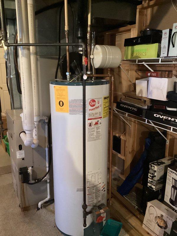 Performed evaluation of existing standard tank water heater installation for potential replacement with tankless system. Current unit is a conventional cylindrical tank model with copper supply lines installed in basement utility area. Documented surrounding clearances, existing plumbing configuration, and ventilation requirements to determine feasibility of tankless conversion.