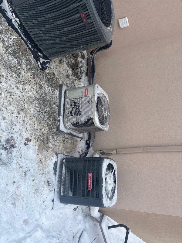 Completed installation of three Trane HVAC condenser units on concrete pad against exterior stucco wall. Units were properly mounted with appropriate refrigerant and condensate lines connected, and control thermostat was installed on the wall above. Photos documented the completed installation showing all three units in place with proper spacing and connections.