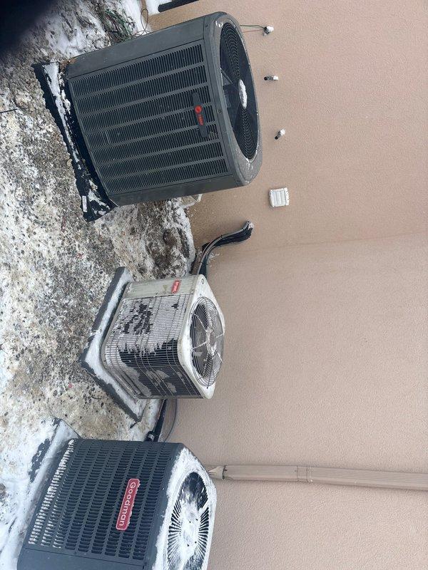 Completed installation of three Trane HVAC condenser units on concrete pad against exterior stucco wall. Units were properly mounted with appropriate refrigerant and condensate lines connected, and control thermostat was installed on the wall above. Photos documented the completed installation showing all three units in place with proper spacing and connections.