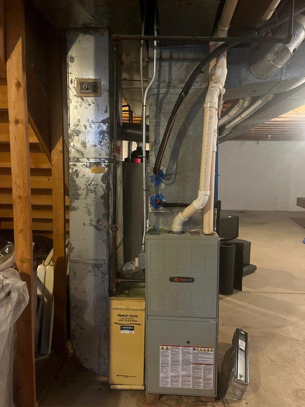 Conducted assessment for furnace and AC retrofit in residential basement. Existing installation includes a Trane air handler with connected ductwork, alongside water heater and various PVC piping. Evaluation focused on replacement options for complete HVAC system upgrade while utilizing current duct configuration.