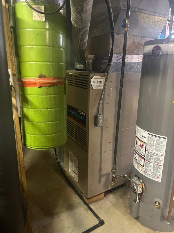 Completed furnace retrofit in residential basement utility room, replacing an aging York system that showed significant water damage and rust. The installation included proper connection to existing ductwork while maintaining connections to the adjacent Rheem water heater and lime-green humidifier tank.