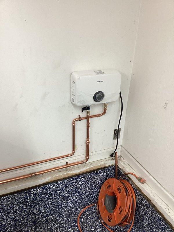 Successfully installed point-of-use Bosch water heater with proper copper pipe connections. Completed vent piping repairs to ensure proper ventilation. Installed utility sink with gooseneck faucet and stainless steel basin on black metal frame.