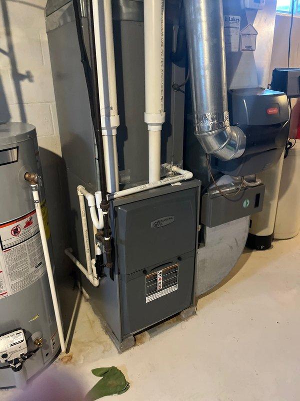 Conducted assessment of 15-year-old furnace for potential replacement. Inspection revealed aging unit with standard efficiency located in basement utility room alongside water heater. Evaluated existing ductwork, PVC venting system, and nearby plumbing to determine compatibility with modern replacement options. Photos documented current installation configuration to facilitate accurate replacement quote.