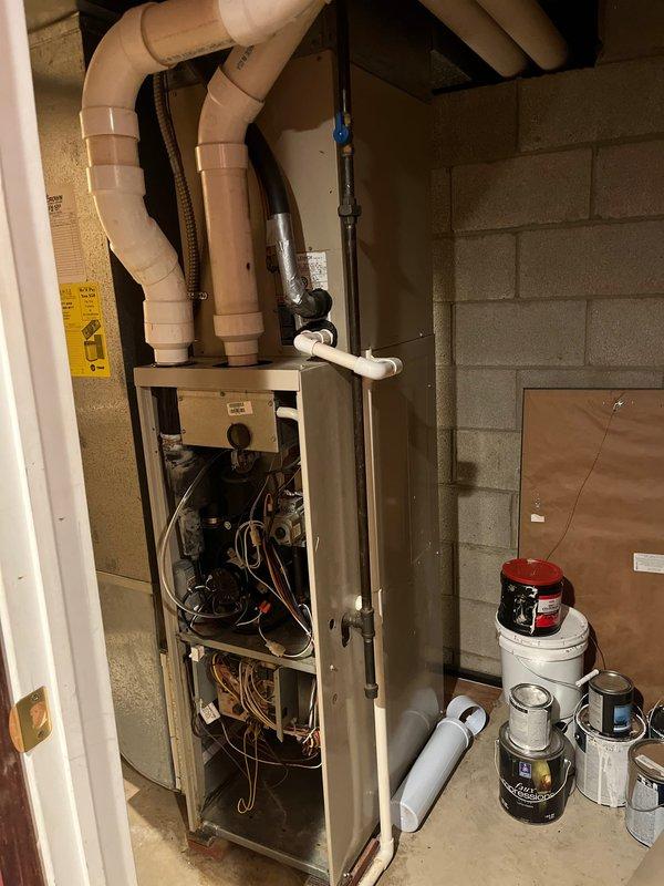 Performed inspection of existing furnace system in basement utility area, revealing exposed internal wiring and components requiring replacement. Evaluated current ventilation setup consisting of PVC piping with multiple bends and joints connected to the ceiling joists. Recommended complete replacement of aging furnace unit to address safety concerns and improve system efficiency.