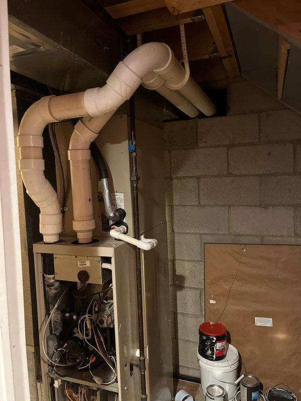 Performed inspection of existing furnace system in basement utility area, revealing exposed internal wiring and components requiring replacement. Evaluated current ventilation setup consisting of PVC piping with multiple bends and joints connected to the ceiling joists. Recommended complete replacement of aging furnace unit to address safety concerns and improve system efficiency.