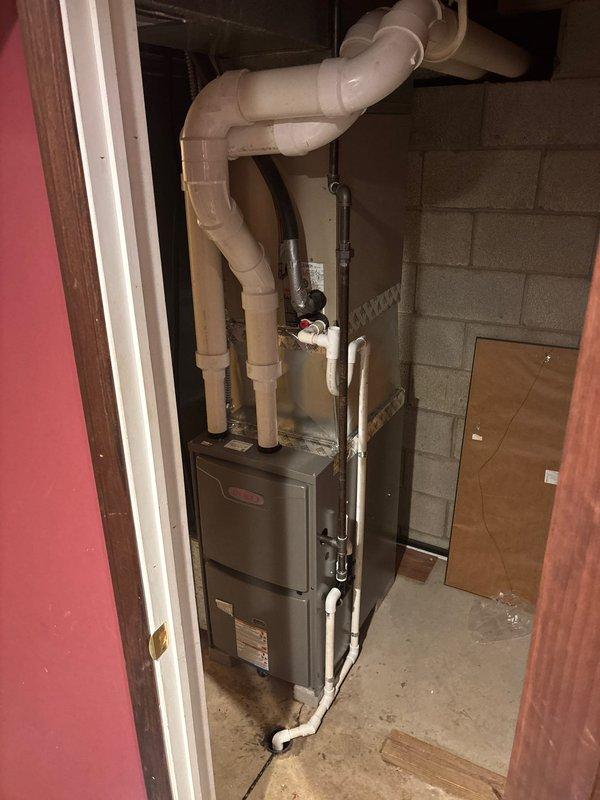 Completed furnace retrofit installation in utility room, replacing existing unit with new metallic HVAC system. Installed proper PVC exhaust ventilation with multiple joints extending upward from the unit, and connected condensate drain line along the furnace side to ensure proper drainage.