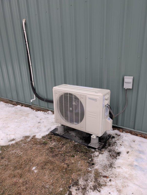 Completed installation of a Perfect Air mini-split system in commercial space with wood-paneled walls and drop ceiling. Replaced existing equipment with new outdoor condensing unit mounted on concrete pad with proper electrical connections and insulated refrigerant lines. Indoor wall-mounted head unit was properly secured and connected for optimal airflow in the workspace.