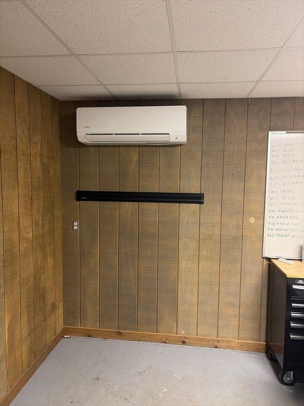 Completed installation of a Perfect Air mini-split system in commercial space with wood-paneled walls and drop ceiling. Replaced existing equipment with new outdoor condensing unit mounted on concrete pad with proper electrical connections and insulated refrigerant lines. Indoor wall-mounted head unit was properly secured and connected for optimal airflow in the workspace.