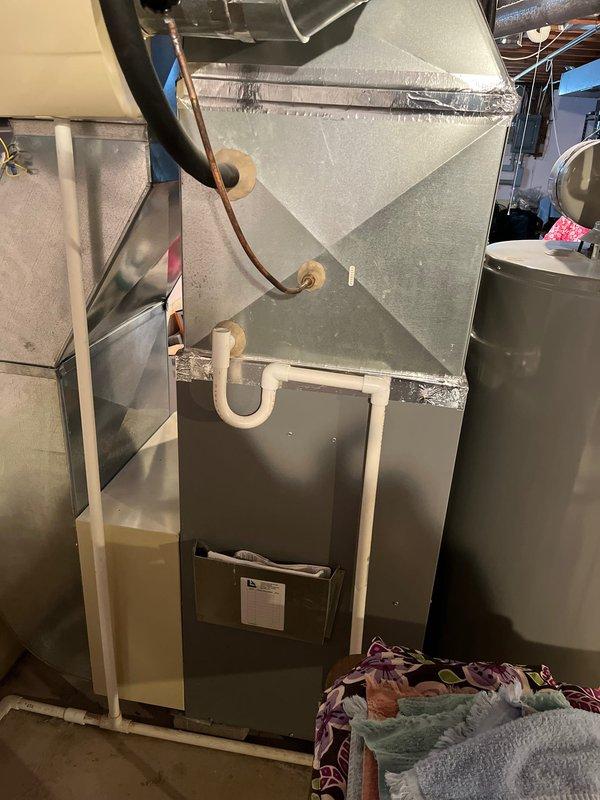 Completed inspection of existing HVAC system in basement utility room. System appears to be a standard furnace unit with connected metal ductwork, plenum, and PVC condensate drain assembly. Observed proper installation of ductwork joints with appropriate metallic sealing tape. Noted presence of humidifier control components and verified proper connection to water heater system.