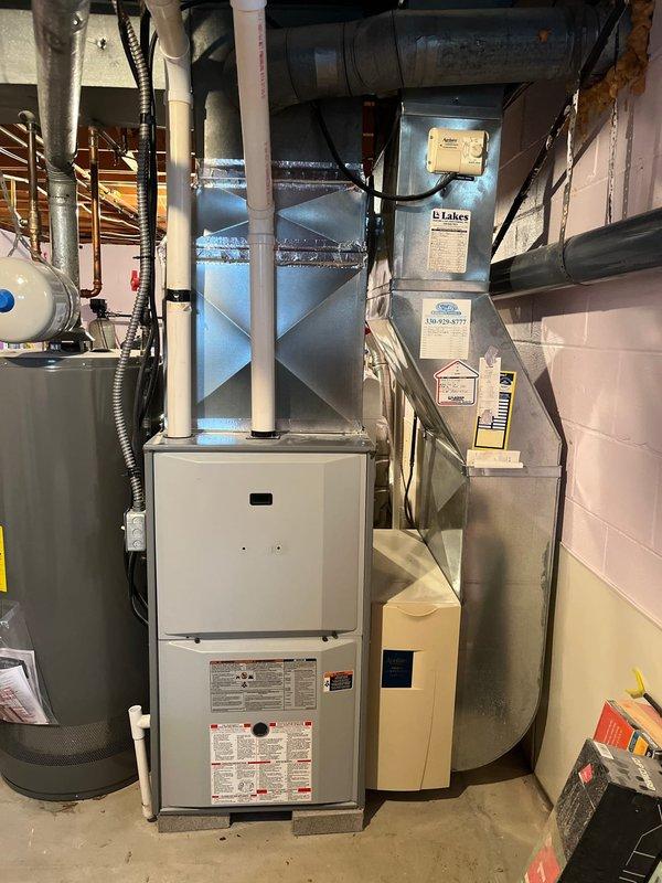 Completed inspection of existing HVAC system in basement utility room. System appears to be a standard furnace unit with connected metal ductwork, plenum, and PVC condensate drain assembly. Observed proper installation of ductwork joints with appropriate metallic sealing tape. Noted presence of humidifier control components and verified proper connection to water heater system.