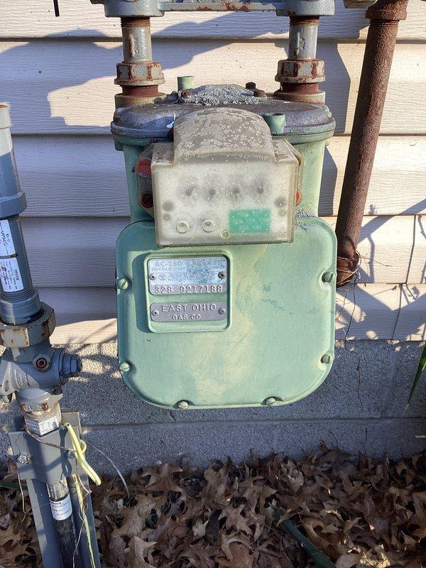 Conducted site assessment for potential tankless water heater installation. Inspected existing gas meter showing signs of corrosion and weathering with "EAST OHIO GAS CO." identification. Evaluated basement infrastructure including exposed ceiling joists, support beams, and existing ductwork to determine appropriate installation location and required modifications.
