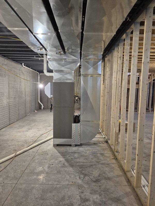 Completed measurement of basement HVAC system installation featuring newly installed metal ductwork throughout the unfinished space. Documented the air handler/furnace unit positioned on concrete flooring with proper connections to the overhead distribution system. Photos captured the current state of installation with exposed framing and electrical components for reference.