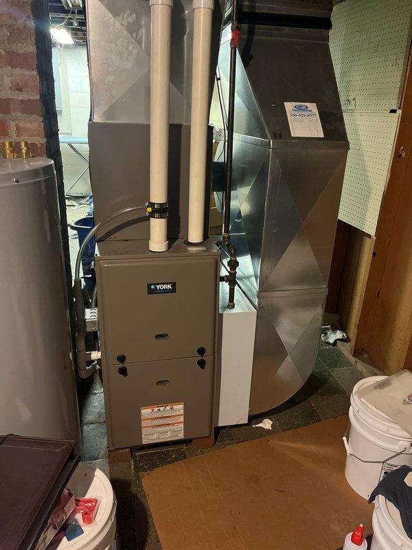 Successfully completed retrofit installation of a York furnace system in basement utility area, including proper connection of dual PVC intake/exhaust ventilation pipes and integration with existing ductwork. System was installed against brick wall with all necessary components including humidifier attachment and properly vented exhaust system.