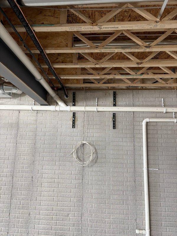 Completed installation of a new HVAC system in an unfinished basement with exposed wooden structural elements. Work included mounting the air handler/furnace unit, installing metal rectangular ductwork along the ceiling joists, and connecting all required PVC venting and electrical components. System was properly secured to concrete block wall with appropriate brackets and all connections were verified to be secure and operational.