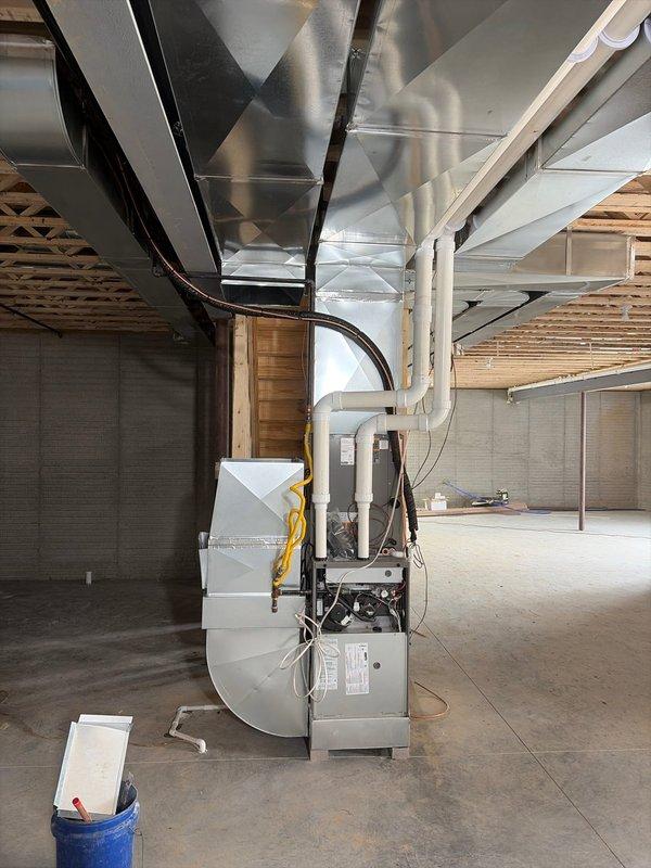 Completed installation of a new HVAC system in an unfinished basement with exposed wooden structural elements. Work included mounting the air handler/furnace unit, installing metal rectangular ductwork along the ceiling joists, and connecting all required PVC venting and electrical components. System was properly secured to concrete block wall with appropriate brackets and all connections were verified to be secure and operational.