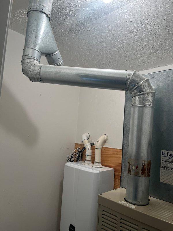 Conducted inspection of existing HVAC system and evaluated potential full system replacement. Documented current installation showing galvanized steel ductwork with L-shaped configuration and connections to existing furnace. Noted presence of Navien tankless water heater mounted on wooden backing with associated copper and PVC plumbing connections that would need to be considered during system replacement planning.