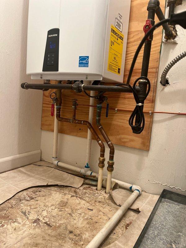 Conducted inspection of existing HVAC system and evaluated potential full system replacement. Documented current installation showing galvanized steel ductwork with L-shaped configuration and connections to existing furnace. Noted presence of Navien tankless water heater mounted on wooden backing with associated copper and PVC plumbing connections that would need to be considered during system replacement planning.