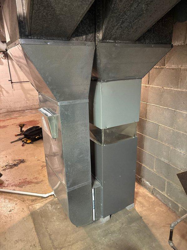 # HVAC Install - Furnace Retrofit

Completed full furnace retrofit installation in residential basement mechanical room. Installed new Lennox furnace unit with matching air handler system, positioned on concrete floor against prepared wall surface. Configured and connected white PVC venting system with proper routing through ceiling penetrations to exterior termination points per manufacturer specifications and local code requirements.

Installed new galvanized metal ductwork system including main vertical trunk line with rectangular transitions and horizontal branch connections to existing floor joist distribution network. Fabricated and secured all duct connections with proper sealing to ensure system efficiency and minimize air leakage. Connected black flexible ductwork sections between rigid components to accommodate equipment vibration and allow for thermal expansion.

Integrated copper refrigerant lines along wall with appropriate pressure gauges and service valves for system mon