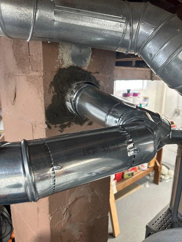 Installed flexible metallic liner material through existing masonry wall penetration to connect HVAC ductwork between utility area and adjacent space. Secured all flexible duct connections with metal clamps and banding to ensure proper airflow and system integrity. Documented completed installation with photographs showing proper routing and connection of black cylindrical duct sections to galvanized ductwork through basement wall opening.