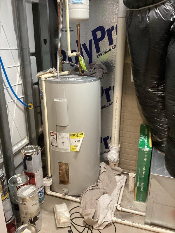 Installed new white cylindrical tanked water heater in residential utility room. Connected copper supply lines with brass fittings and flexible metal connector at top of unit, installed white expansion tank above water heater, and completed all necessary plumbing connections including shut-off valves at base of unit. Unit properly positioned with reflective insulation backing and all manufacturer labels visible for future reference.
