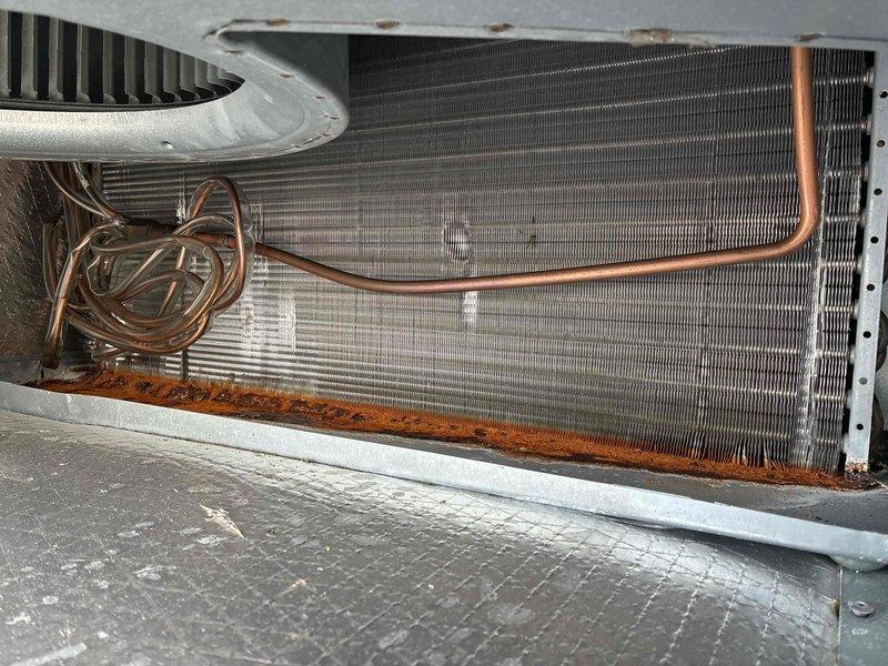 Completed spring/summer preventive maintenance on commercial cooling system. Performed comprehensive inspection of heat exchanger coil assembly, refrigerant lines, and blower components. During inspection, identified significant rust and corrosion at base of heat exchanger unit, particularly at tube connection points and lower platform areas. Corrosion exhibits orange-brown deposits with areas of darker discoloration, indicating prolonged moisture exposure affecting critical connection points. Additional rust damage observed along bottom edge of coil assembly spanning width of unit. Documented conditions with photographic evidence. Verified refrigerant line integrity and blower fan housing condition. Advised customer of corrosion findings and recommended monitoring for potential replacement needs to prevent system failure. Unit operational at time of service completion.
