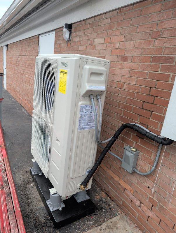 Completed installation of a new split-system heat pump with side discharge outdoor unit and air handler in attic space. The outdoor unit (model BZ33-INV600UT2-454-G3-J) was mounted on a composite pad against the building exterior with properly routed refrigerant lines and electrical connections, including disconnect box installation. All system components were installed per manufacturer specifications with 208/230V single-phase power supply, 40-amp circuit protection, and IPX4 water ingress protection rating.