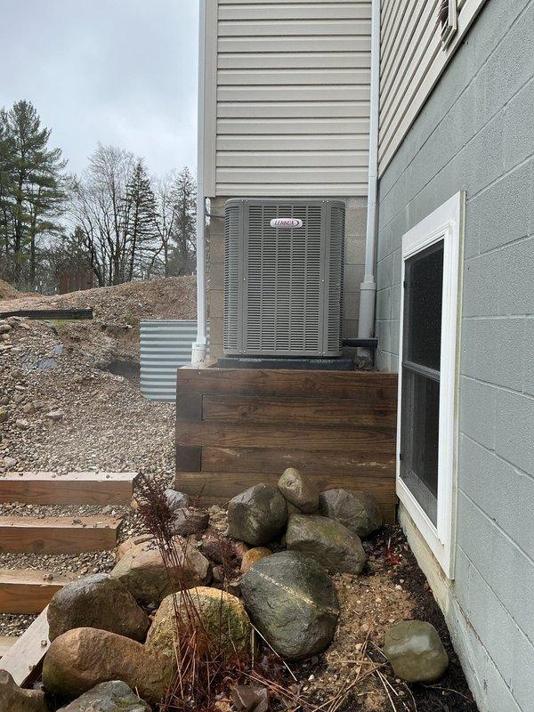 Completed new construction HVAC installation including Lennox condenser unit mounted on exterior platform with proper PVC condensate drainage routing along building exterior. Interior basement installation features furnace with connected ductwork and air handler, all mechanical systems commissioned and operational with power confirmed via LED indicators.